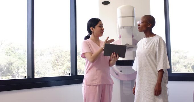 Imaging tech using tablet, explaining mammogram prep to African American patient at mammogram unit