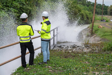 A engineering doing his checking routine. He is wearing hard hat and engineer uniform.Standing by the rail by the dam.Monitor water levels from the heavy rain that has been falling for several days.