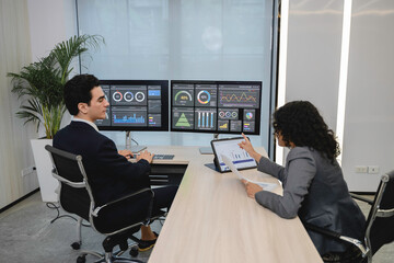 Business professionals analyzing data and discussing financial reports with digital dashboards and graphs in a modern office setting, focusing on strategy and performance.