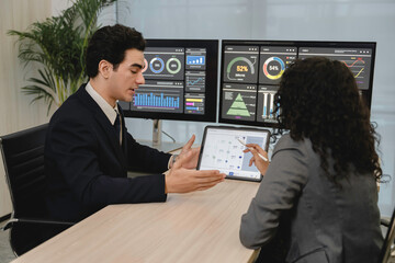 Business professionals analyzing data and discussing financial reports with digital dashboards and graphs in a modern office setting, focusing on strategy and performance.