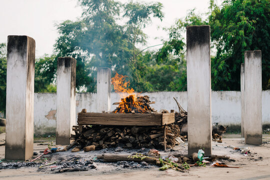 a Hindu outdoor funeral pyre burning on a wooden bier at a rural cremation ground in India, frontal wide view of the concrete platform