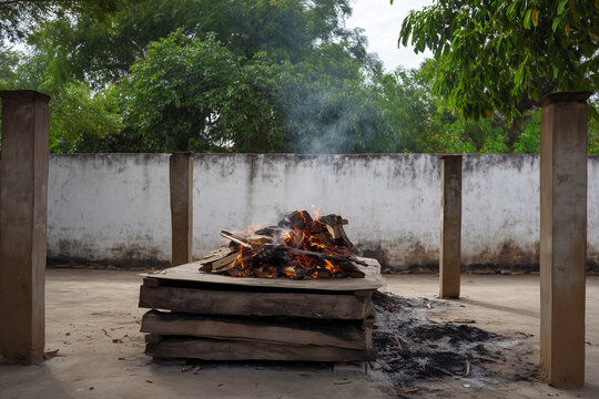 a Hindu outdoor funeral pyre burning on a wooden bier at a rural cremation ground in India, frontal wide view of the concrete platform 
