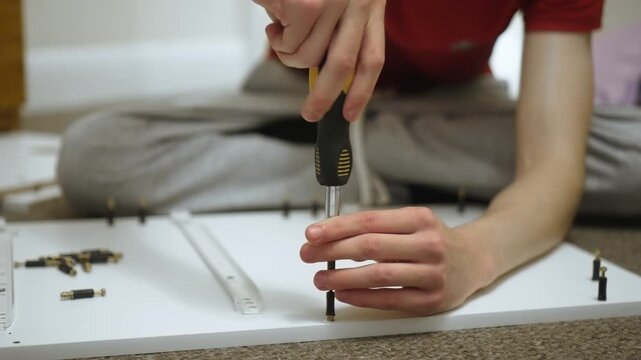 Aligning assembly dowel on drawer panel during dresser assembling. Positioning fastening connector on furniture board while crafting DIY cabinet. Adjusting hardware element on woodworking project