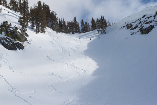 Striking alpine scene in a snowy mountain bowl featuring winding ski tracks descending the right side of the slope, contrasted by clusters of roller balls (snow rollers) forming on the left under sun.