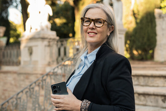 Smiling businesswoman holding smartphone in a park in Rome