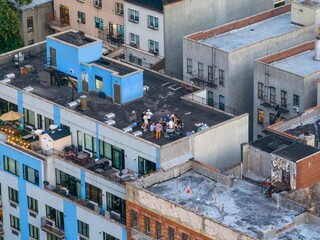 Aerial view of rooftops hosting casual gatherings under the open sky, a tapestry of textures and tones contrasting against the urban landscape, New York, New York, United States.