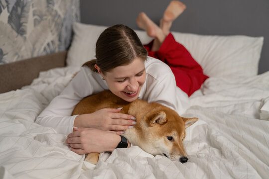 Woman cuddling her Shiba Inu on a cozy bed