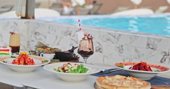 Luxurious poolside dining spread featuring gourmet dishes and refreshing drinks at a high-end resort with a sparkling blue swimming pool. Upscale vacation, culinary experience, summer indulgence