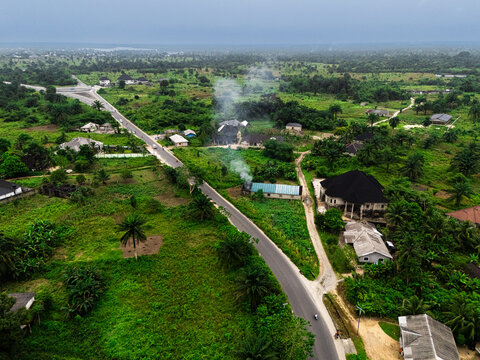 Aerial view of a road cutting through lush greenery, with sparse buildings and smoke rising into the sky, Gokana, Rivers, Nigeria.