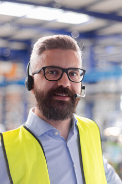 Production manager using headset calling, standing in modern industrial factory.