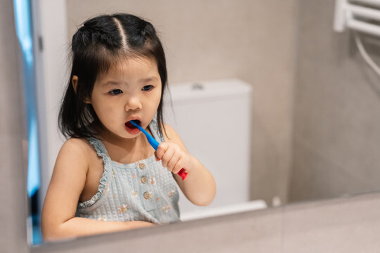 Young child learning to brush teeth in bathroom