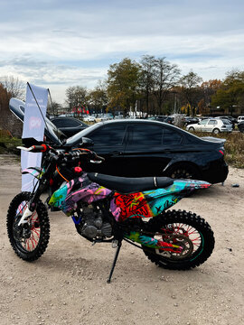 Colorful graffiti  Geon Dakar GNS 300 motorcycle on display at an outdoor event with a crowd and cars