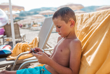 Boy relaxing on beach lounger playing game on smartphone.