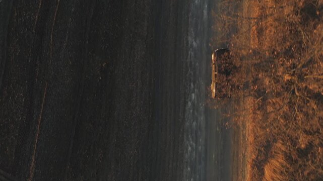 Flying over off road vehicle moving on route near farmland. Aerial shot of pickup truck driving through rural path near ploughed field. Black car moving along road near plowed meadow at autumn