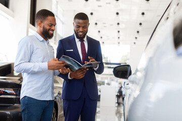 Black Car Seller Showing Catalog With Vehicle Models To Male Customer In Dealership Center,...
