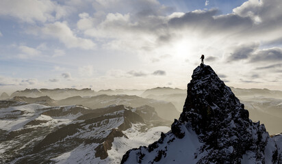 Fototapeta premium Climber Standing On Snowy Mountain Peak With Sunrise Over Vast, Misty Range