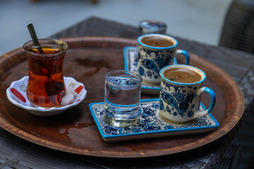 Obraz premium Traditional Turkish tea in a tulip glass and Turkish coffee in ornate ceramic cups served on a wooden tray with water. Authentic Mediterranean cafe culture. September, Antalya region, Turkey.