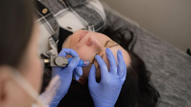 Professional master performing eyeliner tattoo procedure in beauty salon