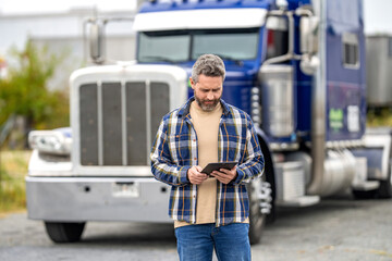 Hispanic trucker at truck. Using tablet chatting with customer. Service diagnostics for truck. Man use tablet to configure equipment. Trucker driver man with tablet control loading. Truck maintenance
