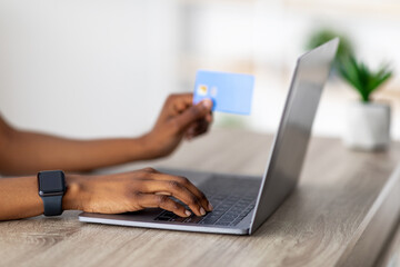 Online sale, remote shopping. Unrecognizable black woman with credit card and laptop typing on keyboard, buying on web at home. Closeup of Afro lady purchasing goods in internet
