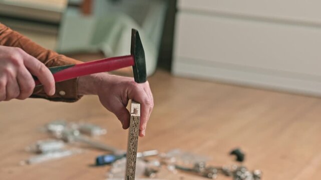 Skilled individual using a hammer to drive a nail into a wooden piece on a workshop floor surrounded by various tools and materials showcasing the crafting process