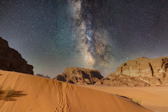 Wadi Rum desert, Jordan. Stars shine over desert landscape with sand dunes, mountains in night sky