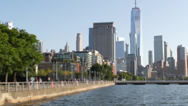 New York City Manhattan downtown financial district skyline, United States. Urban waterfront cityscape, World Trade Center skyscraper building, Hudson River Park, people walk on riverfront promenade.