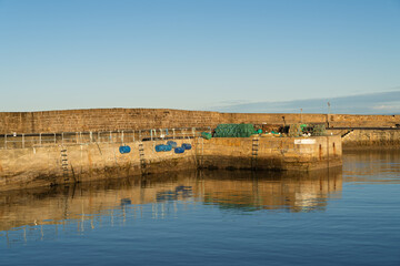 Fototapeta premium Golden hour sunlight shines on quay at Hopeman Harbour revealing still water reflections