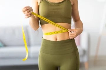 Fotobehang Diamanten Cropped view of slim Indian woman measuring her waist with tape measure at home, closeup. Unrecognizable Asian lady checking result of weight loss diet or liposuction indoors  © Prostock-studio