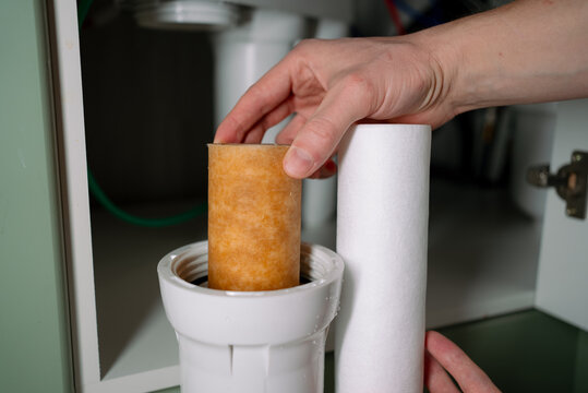 Person changing a dirty residential water filter cartridge with a clean one, performing essential maintenance on a home reverse osmosis water purification system for improved drinking water quality