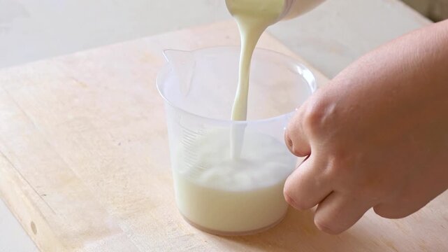 Female hands pouring white milk into the measure cup