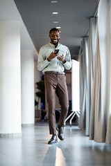 Fototapeta premium Young man walking and using smartphone in office corridor
