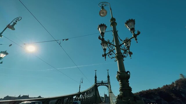Scenic view of the green Liberty Bridge in Budapest, Hungary, over the Danube. Traffic with yellow trams crosses the historic steel structure under a clear sunny blue sky.

