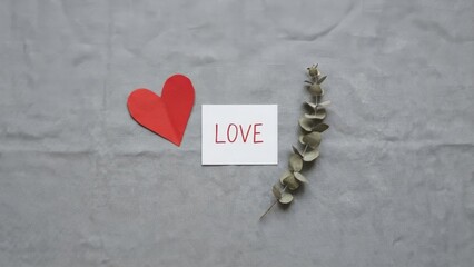 Small red paper heart and a love note on a grey linen background.