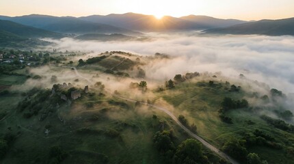 Thick fog rolling over mountain valley at sunrise. Misty landscape with village houses and winding road through green hills. Serene natural scenery for atmospheric nature photography.