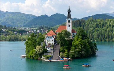 Fototapeta premium Aerial drone view of Bled Island with the Church of the Assumption in the middle of Lake Bled, Slovenia. The iconic island church is surrounded by turquoise alpine waters and forested mountains. Famou