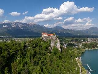 Aerial view of Bled Castle overlooking Lake Bled, Slovenia. Medieval fortress on a cliff captured by drone, surrounded by alpine landscape and clear blue water. Famous European travel destination and 