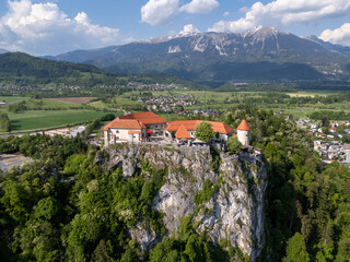 Aerial view of Bled Castle overlooking Lake Bled, Slovenia. Medieval fortress on a cliff captured by drone, surrounded by alpine landscape and clear blue water. Famous European travel destination and 
