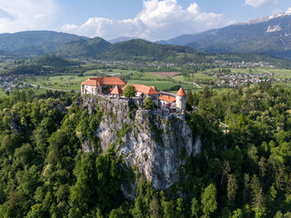 Aerial view of Bled Castle overlooking Lake Bled, Slovenia. Medieval fortress on a cliff captured by drone, surrounded by alpine landscape and clear blue water. Famous European travel destination and 