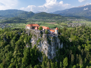 Aerial view of Bled Castle overlooking Lake Bled, Slovenia. Medieval fortress on a cliff captured by drone, surrounded by alpine landscape and clear blue water. Famous European travel destination and 