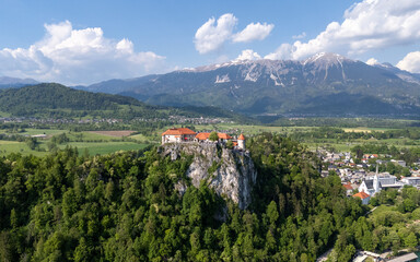 Aerial view of Bled Castle overlooking Lake Bled, Slovenia. Medieval fortress on a cliff captured by drone, surrounded by alpine landscape and clear blue water. Famous European travel destination and 