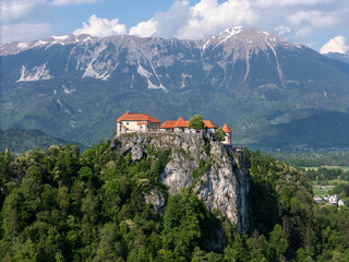 Aerial view of Bled Castle overlooking Lake Bled, Slovenia. Medieval fortress on a cliff captured by drone, surrounded by alpine landscape and clear blue water. Famous European travel destination and 
