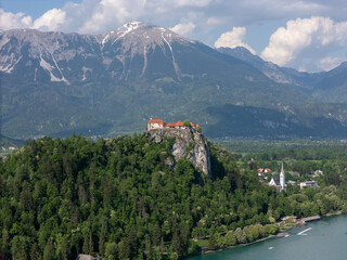 Aerial view of Bled Castle overlooking Lake Bled, Slovenia. Medieval fortress on a cliff captured by drone, surrounded by alpine landscape and clear blue water. Famous European travel destination and 