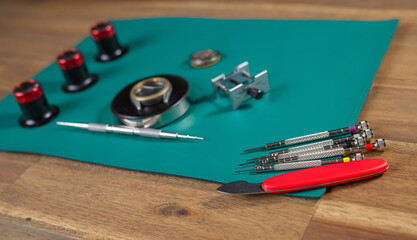 A watchmaker prepares tools for the repair of a mechanical watch on a green surface with various instruments.