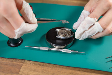 Professional watchmaker focuses on careful assembly and repair of a mechanical watch movement using fine tools on a workbench.