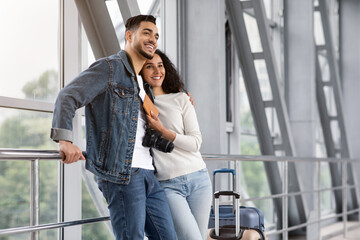 Fototapeta premium Family Trip. Romantic Arab Couple Waiting For Flight In Airport Lounge Zone, Happy Young Middle Eastern Spouses Travelling Together, Standing With Luggage And Embracing In Terminal, Copy Space