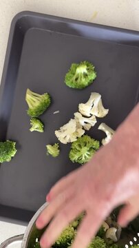 Seasoning a Sheet Pan of Broccoli and Cauliflower Vegetable Shot from Above