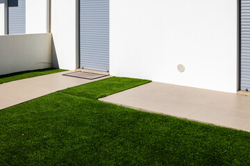 Minimalist residential building entrance with white facade roller shutters tiled walkway and green artificial grass in a modern coastal town, Portugal, Torreira, 13 October 2025