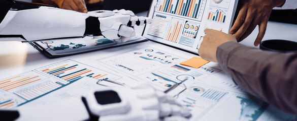 Human and robotic hands engage in a collaborative analysis of business data, showcasing graphs and charts in a modern office setting, emphasizing innovation and teamwork.Noogenesis