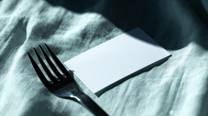 Blank white card placed next to a silver fork on a soft, textured green fabric, presenting a clean layout for custom text or menu